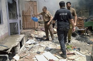 Sur cette photo fournie par le bureau de la police du district, un officier de police verse de l'eau dans une maison en feu dans un quartier chrétien à la suite d'une attaque d'une foule en colère à Jaranwala, près de Faisalabad, au Pakistan.